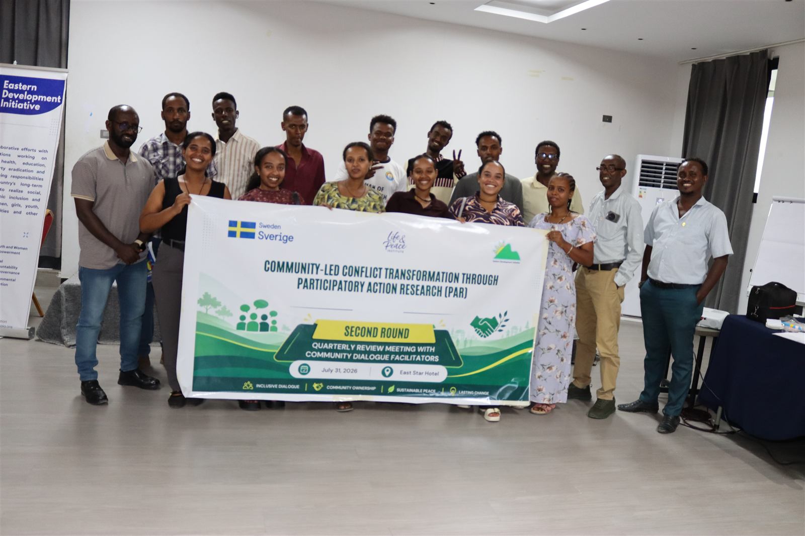 Facilitators holding the Second Round Quarterly Review Meeting banner, July 2026