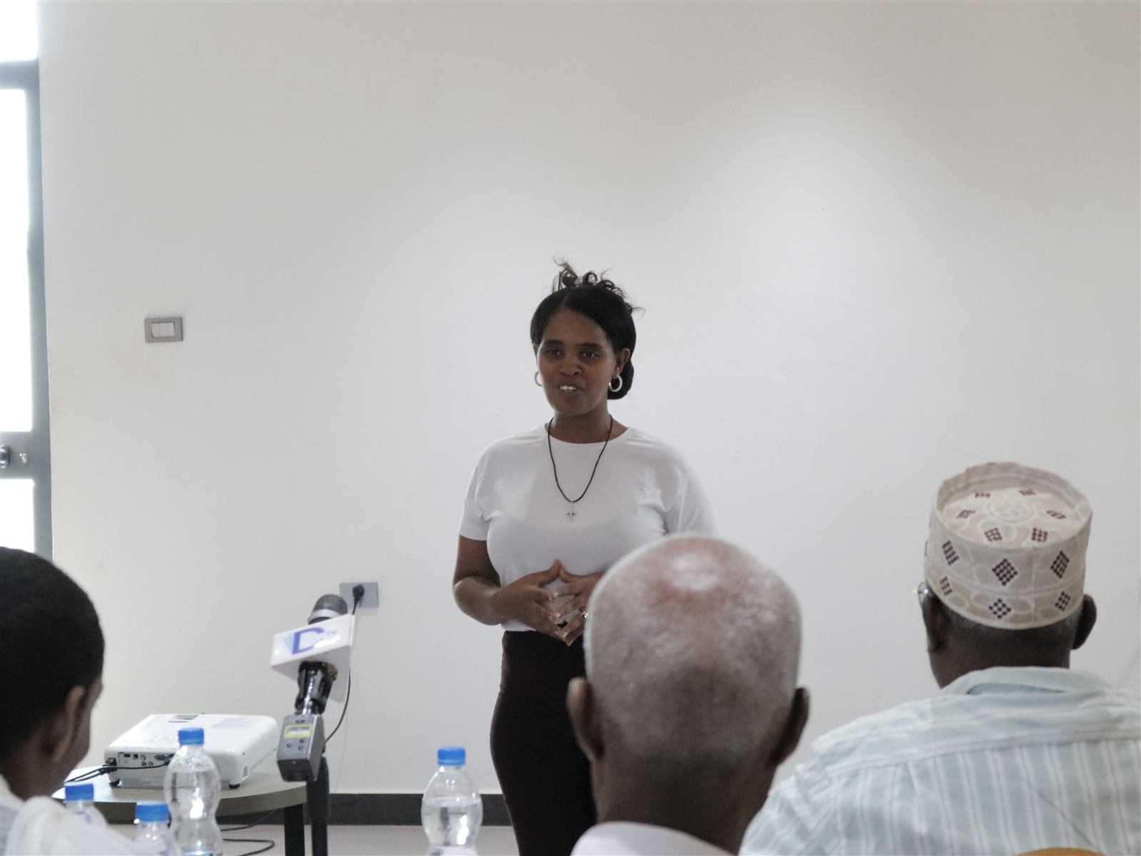 Facilitator addressing seated participants, including a religious leader in a woven cap