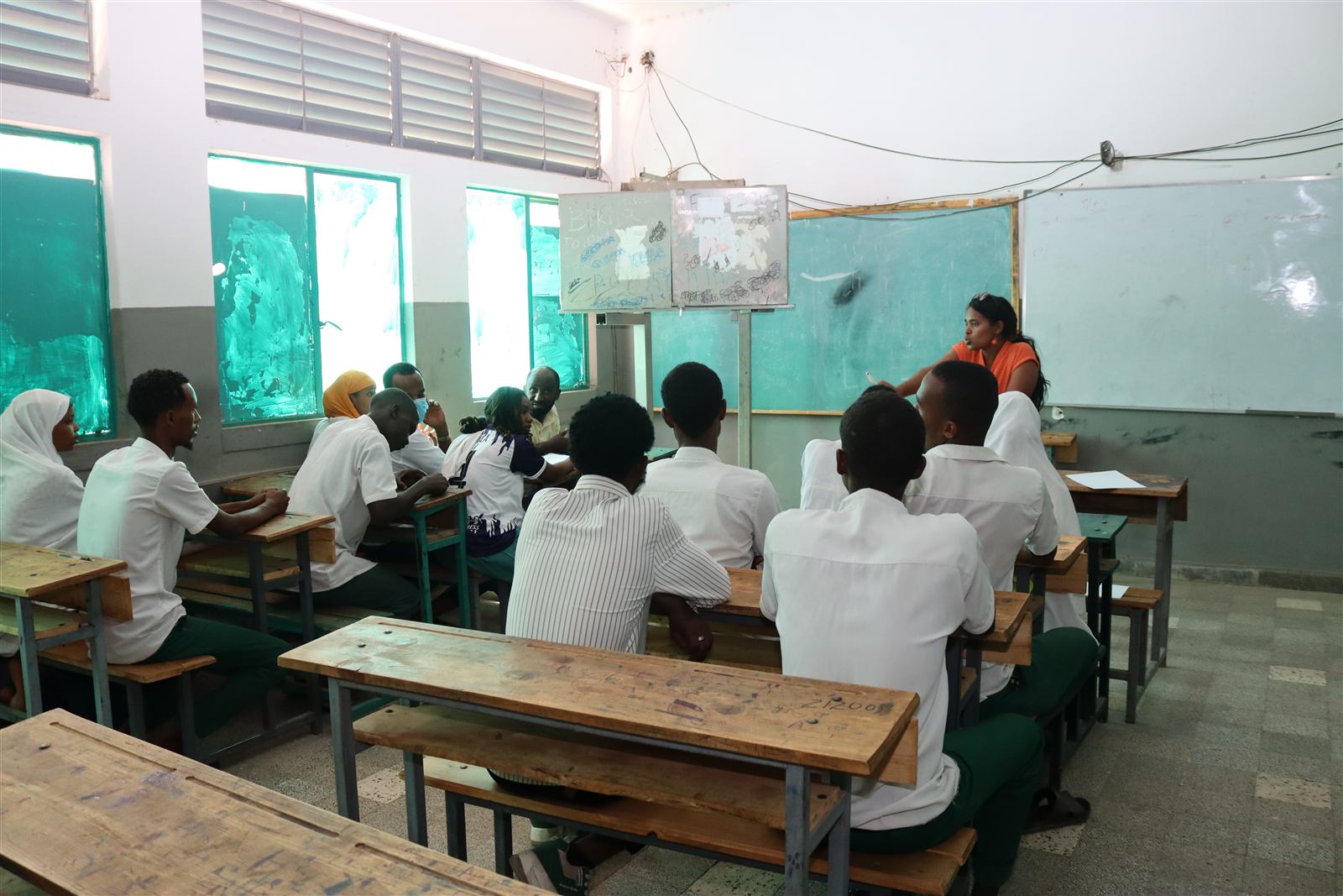 Classroom scene with students in uniform and an EDI facilitator teaching at the chalkboard