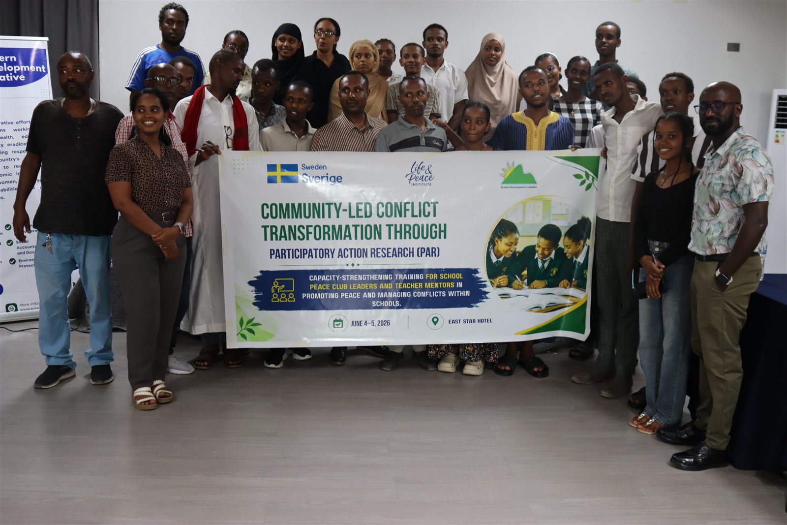 Closing group photo of about thirty participants holding the full training banner with the Sweden, Life and Peace Institute, and EDI logos