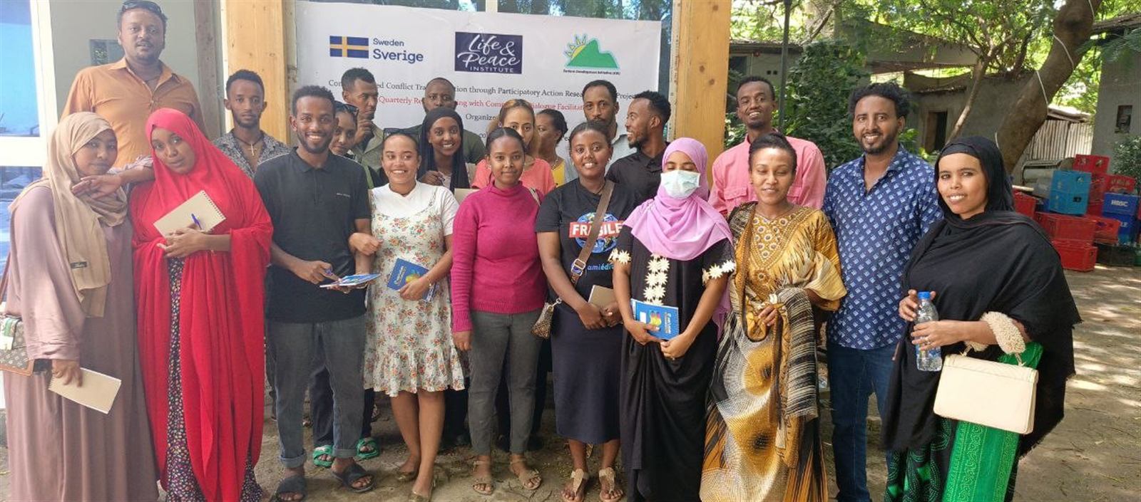 Program staff and partners together outside, holding the Sweden, Life and Peace Institute, and EDI event banner