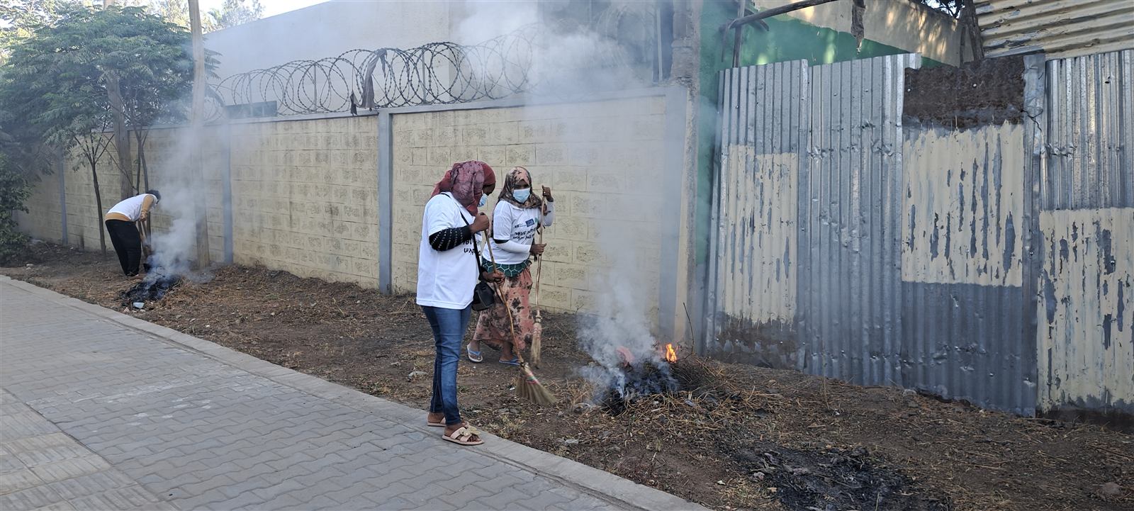 Participants gathered near a small burning pile of cleared debris, smoke rising