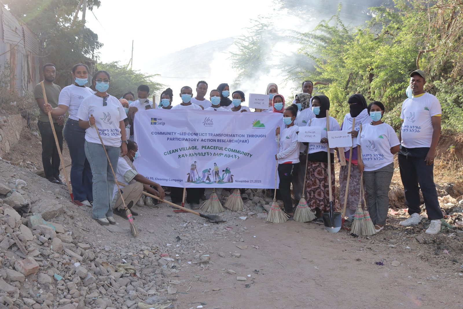 About twenty participants, a majority of them women in headscarves, holding brooms, shovels, and handwritten Amharic signs behind the full PAR campaign banner